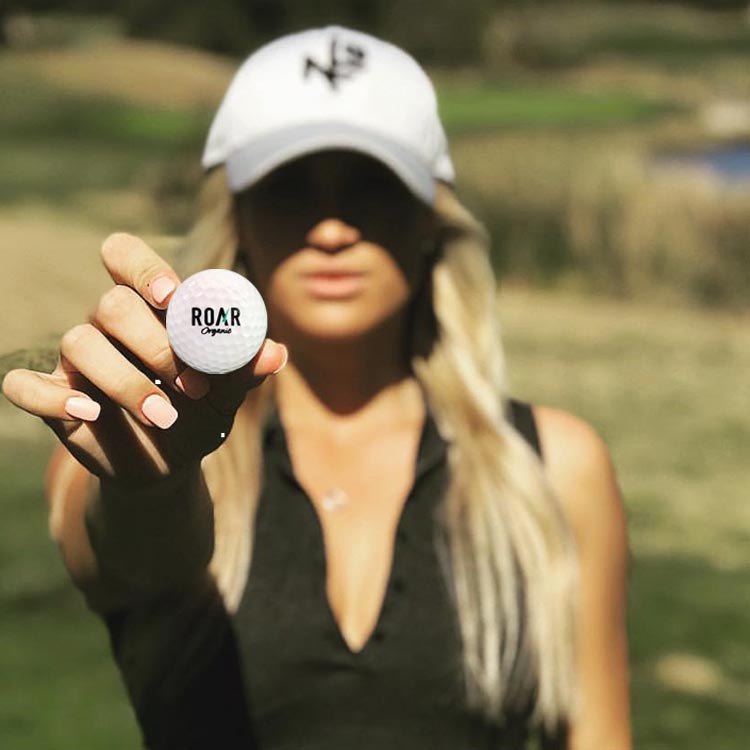 Woman Golfer Holding a Custom Golf Ball With a ROAR Logo on It