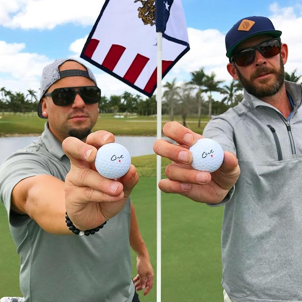 Two Golfer Holding Cut DC Golf Balls In Front of Them Next to the Pin