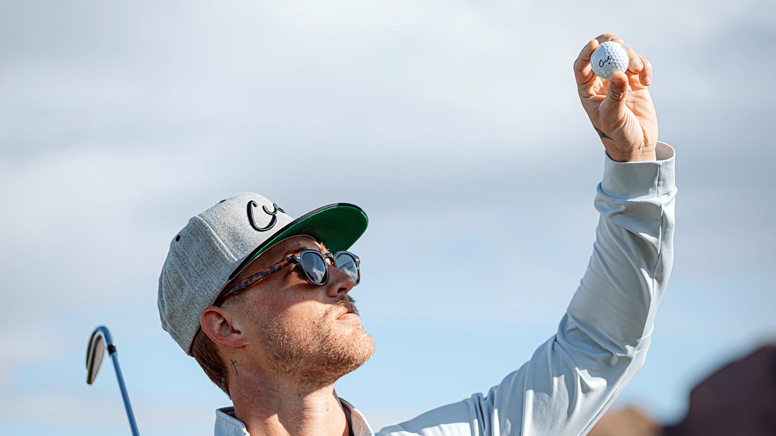 Golfer Wearing a Cut Golf Balls Hat Holding Up a Cut Ball With Ball Logo Facing Camera