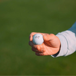 Golfer Holding Cut Grey Ball In Right Hand With Logo Showing